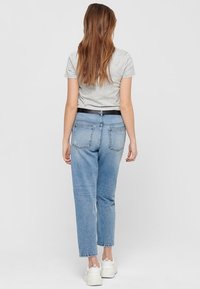 Světle šedá košile s krátkým rukávem kombinovaná s modrými džíny s vysokým pasem. Džíny mají rovný střih nohavic a dvě zadní kapsy. Na nohách bílé tenisky.