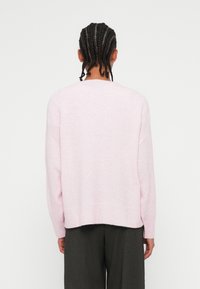 Απαλή ροζ πλεχτή μπλούζα με χαλαρή γραμμή, ραμμένο στρίφωμα και μακριά μανίκια. Λείος υφασμάτινος χαρακτήρας, στρογγυλή λαιμόκοψη και μινιμαλιστικός σχεδιασμός.