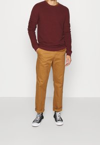 Bordeaux rode geribbelde trui met een ronde hals, gecombineerd met beige chino's en zwarte hoge sneakers met witte zolen.