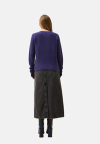 Lila gerippter Pullover mit langen Ärmeln, kombiniert mit einem dunkelblauen Jeans-Midirock mit einem Schlitz auf der Rückseite, getragen mit hohen Blockabsatzstiefeln.