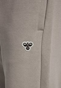 Graue Baumwoll-Jogginghosen mit einem kleinen, gestickten Bienensymbol am oberen Oberschenkel, mit einem strukturierten, glatten Stofffinish.