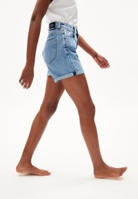 Pantalones cortos de mezclilla azul claro con dobladillos enrollados, que presentan una cintura alta, un diseño clásico de cinco bolsillos y una etiqueta de marca negra en la parte posterior.