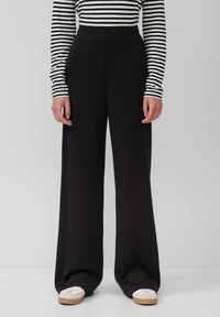 Schwarze, weit geschnittene Hose mit elastischem Bund, aus einem weichen Material, das eine glatte Textur und ein einfaches, klares Design aufweist.