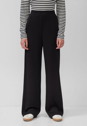 Schwarze, weit geschnittene Hose mit elastischem Bund, aus einem weichen Material, das eine glatte Textur und ein einfaches, klares Design aufweist.