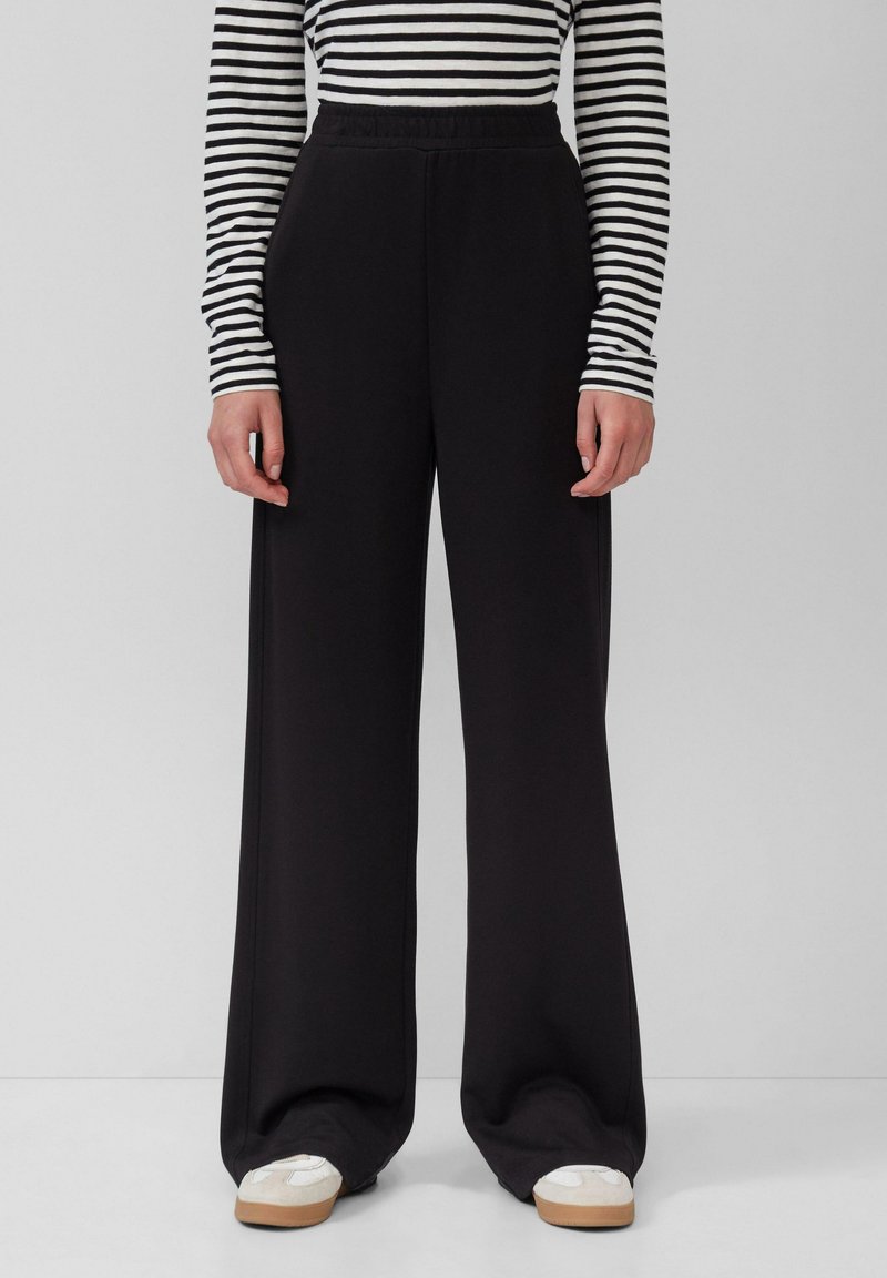 Pantalons larges et noirs avec une taille élastique, fabriqués dans un matériau doux, présentant une texture lisse et un design simple et épuré.