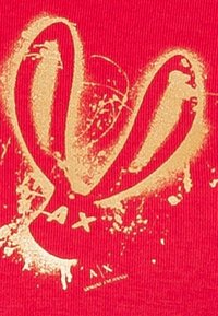 Tissu rouge avec un design abstrait doré présentant une forme en cœur et des effets d'éclaboussure, accompagnés d'un texte supplémentaire en plus petite police.