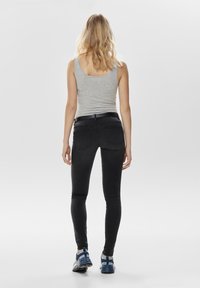 Black slim-fit jeans with a smooth texture, five-pocket design, and stitched detailing. Paired with a gray tank top and blue athletic shoes.