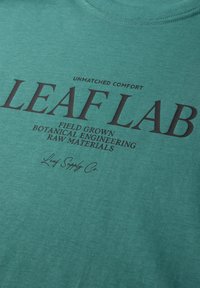 Tissu vert avec texte noir indiquant "LEAF LAB", "Confort inégalé" et "Matériaux bruts d'ingénierie botanique cultivés sur le terrain".