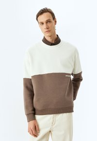 Sudadera con bloques de color, con una parte superior en crema y una sección inferior marrón. Fabricada en material suave, presenta puños acanalados y un pequeño acento de logo.