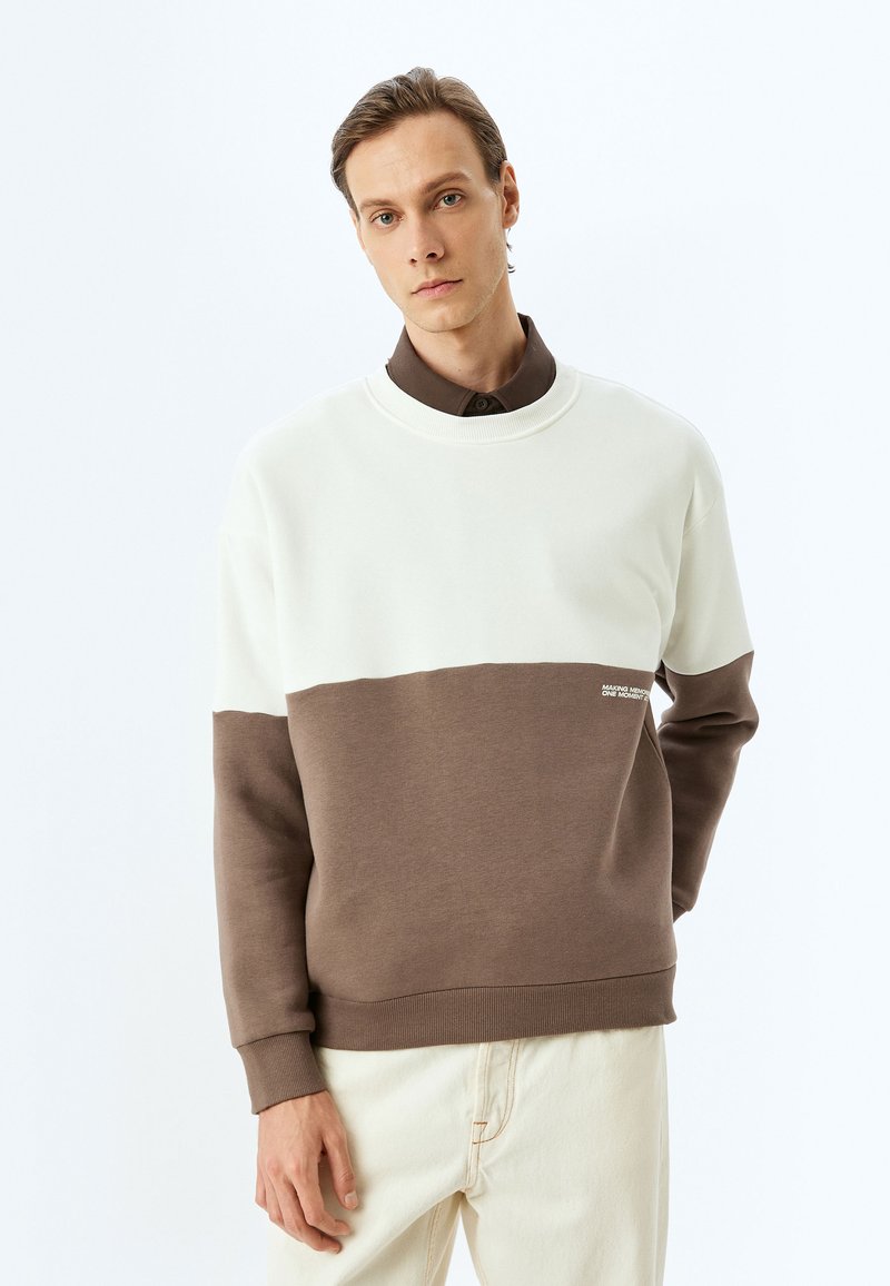 Sudadera con bloques de color, con una parte superior en crema y una sección inferior marrón. Fabricada en material suave, presenta puños acanalados y un pequeño acento de logo.