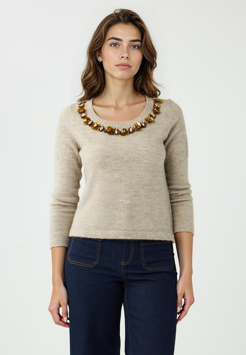 Pull en laine beige à manches trois-quarts et col rond, orné de pierres décoratives dorées et transparentes le long du col.