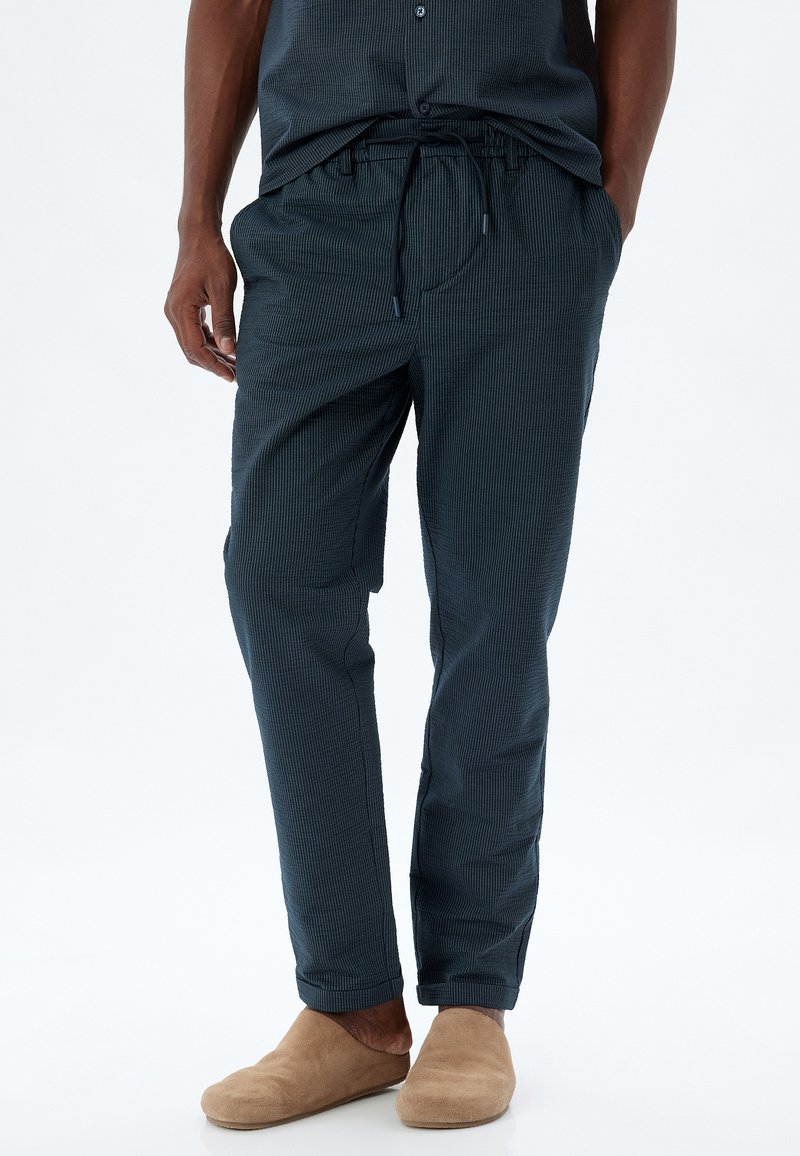 Marinblå randiga byxor i lätt tyg med elastisk midja och dragsnöre, med sidofickor och insvängda ben.