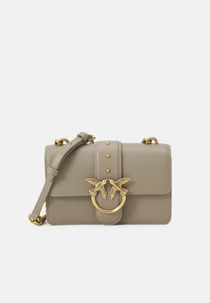 Beige læder skuldertaske med gyldent spænde formet som en fugl og justerbar rem, hviler mod en hvid baggrund.