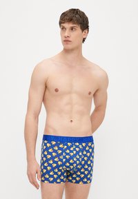 Modré boxerky s opakujúcim sa vzorom žltých gumových kačičiek, s modrým elastickým pásom s nápisom "HAPPY".