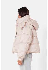 Lys beige pufferjakke med lodrette striber, oversized hætte og sikre lukninger. Har elastiske manchetter og et cropped design.