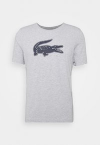 Camiseta de algodón gris con cuello redondo, que presenta un diseño de logo de cocodrilo azul marino en el frente. Mangas cortas y un corte relajado.