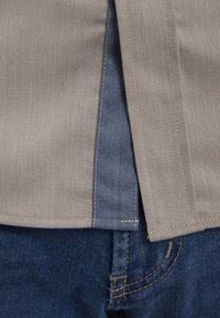 Beiger gestreifter Stoff überlappt dunkelblauen Denim, mit geradem Rand und sichtbaren Nähten, die einen strukturierten Materialkontrast zeigen.