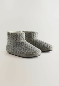 Grå strikkede hjemmesko med et tekstureret chevron-mønster, blød foring og bløde såler. Designet har en lav ankelhøjde for nem påtagning.