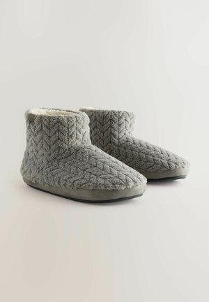Grijze gebreide sloffen met een gestructureerd chevronpatroon, pluizige voering en zachte zolen. Het ontwerp heeft een lage enkelhoogte voor gemakkelijk aan- en uittrekken.