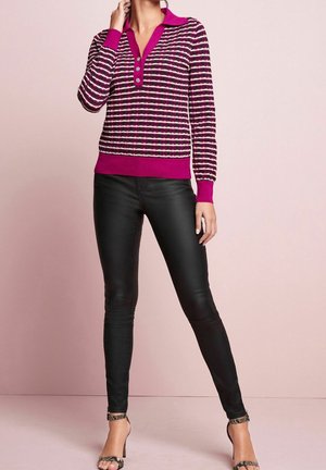 Pull en maille rose et noir avec un col et trois boutons, associé à un pantalon noir slim et des talons à lanières, sur fond rose clair.
