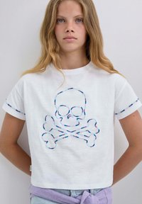 Weißes Baumwoll-T-Shirt mit einem Design von Totenkopf und gekreuzten Knochen, umrandet mit mehrfarbiger Stickerei. Kurze Ärmel mit kontrastierendem Besatz.