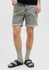 Shorts en denim gris avec des ourlets roulés, associés �à des chaussettes gris clair et des sandales noires à deux sangles. L'arrière-plan est blanc uni.