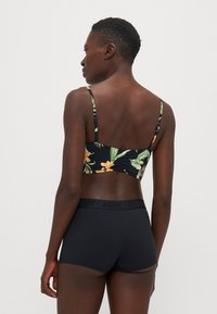Schwarzer floraler Bralette mit dünnen Trägern, der tropische Muster aufweist. Kombiniert mit hoch taillierten schwarzen Shorts mit einem markanten Bund.