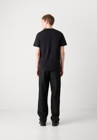 Černé bavlněné tričko s krátkým rukávem, kombinované se volnými tmavě šedými kalhotami. Jednoduchý design, jednotné barvy, žádné viditelné vzory nebo loga.
