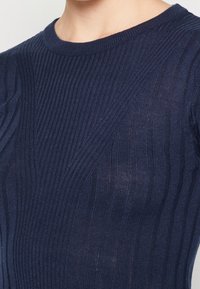 Top en maille côtelée bleu marine avec un col rond et un design texturé, ajusté pour un look fitted.