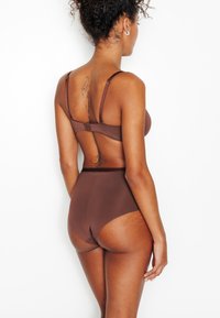Ensemble de lingerie marron comprenant un soutien-gorge sans armatures avec bretelles réglables et un slip taille haute, présentant un tissu lisse et un design minimaliste.