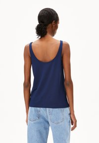 Marineblauwe tanktop met brede bandjes, een ronde hals aan de achterkant en een relaxte pasvorm, gecombineerd met lichtblauwe high-waisted jeans.