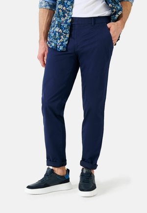Marineblaue Hosen im Slim-Fit, mit einer glatten Textur und umgeschlagenen Säumen, kombiniert mit dunklen Sneakers und einem gemusterten Blumenhemd.