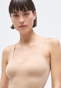 Sutien sport fără cusături, de culoarea pielii, cu bretele late și panouri texturate. Material fin, cu o croială adaptată, proiectat pentru confort și susținere.