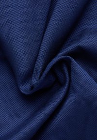 Close-up van dicht geweven donkerblauwe stof met een gladde textuur en subtiele plooien die zachte schaduwen creëren.