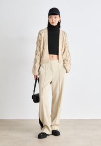 Μπεζ κάρντιγκ με πλέξη καλωδίου, μαύρο ζιβάγκο και κρεμ παντελόνι με πλατινές μπαγκέτες. Η εμφάνιση ολοκληρώνεται με μαύρη τσάντα και χοντρές μαύρες πατούσες.