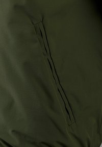 Dunkelgrüner Stoff mit glatter Textur verfügt über eine Seitentasche; die Nähte sind dezent, mit einer vertikalen Naht, die das Design der Tasche akzentuiert.