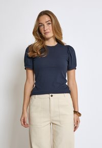 Marinblus med ribbat mönster, kort ärm och rundad halsringning, i kombination med beige högmidjade vida byxor.