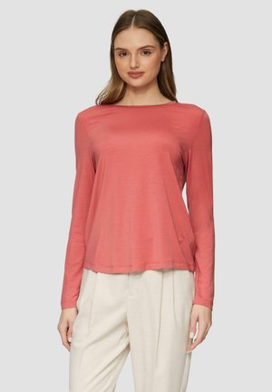 Chemise corail à manches longues en tissu lisse avec une coupe ample, un col rond et des fentes sur les côtés, portée avec un pantalon léger et ample.