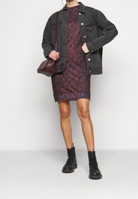 Svart denimjacka över en vinröd leopardmönstrad klänning med ribbad nederkant, kompletterad med svarta snörstövlar och en vinröd axelväska.