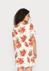 Vestido floral com mangas curtas, cintura ajustada e saia rodada. O tecido é leve e apresenta grandes padrões de flores vermelhas e laranjas sobre um fundo branco.