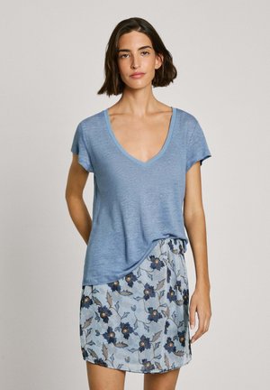 Blaues V-Ausschnitt-T-Shirt mit kurzen Ärmeln, kombiniert mit einem hellblauen Rock mit Blumenmuster, der dunkle Blumen und Blätter zeigt. Lässige Passform.