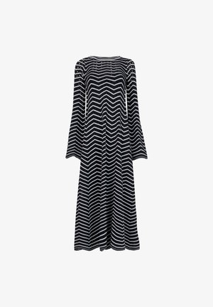 Vestido de manga larga en patrón de zigzag negro y blanco, con un escote redondeado y una tela fluida que cae hasta la mitad de la pantorrilla.