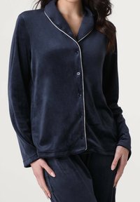 Maglione da pigiama in velluto blu navy con colletto a scialle, piping bianco lungo i bordi e chiusura con bottoni. Maniche lunghe e vestibilità morbida.