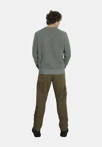 Maglione grigio lavorato a maglia con un motivo testurizzato, abbinato a pantaloni cargo color verde oliva con tasche. Modello di spalle, indossando stivali neri.