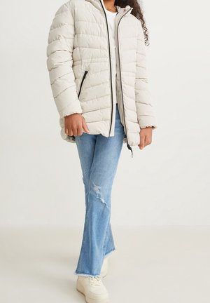 Puffige beige Jacke mit horizontalen Nähten, Frontreißverschluss und Taschen. Kombiniert mit hellblauen, distressed Schlagjeans und weißen Turnschuhen.