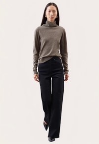 Jasnobrązowy golf z miękkiego materiału, zestawiony z czarnymi spodniami o wysokim stanie i szerokich nogawkach. Czarne buty na obcasie dodają elegancji.