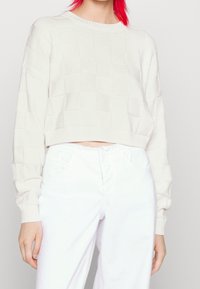 Kort, stickad tröja i off-white med ett mönster av fyrkanter, rund halsringning och ribbade ärmslut, tillsammans med vita denimbyxor.