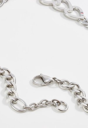 Collier en chaîne argentée avec des maillons entrelacés en forme de cœur et une fermeture à pince homard sur fond blanc.