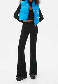 Blå puffväst, svart tajt långärmad topp och utsvängda svarta byxor. Outfiten har släta linjer och en glänsande textur i västen.