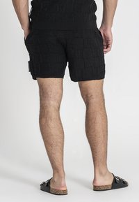 Pantaloni corti neri lavorati a maglia con un design a motivi testurizzati, caratterizzati da una vita a coste e tasche laterali. Indossati con sandali neri senza chiusura.